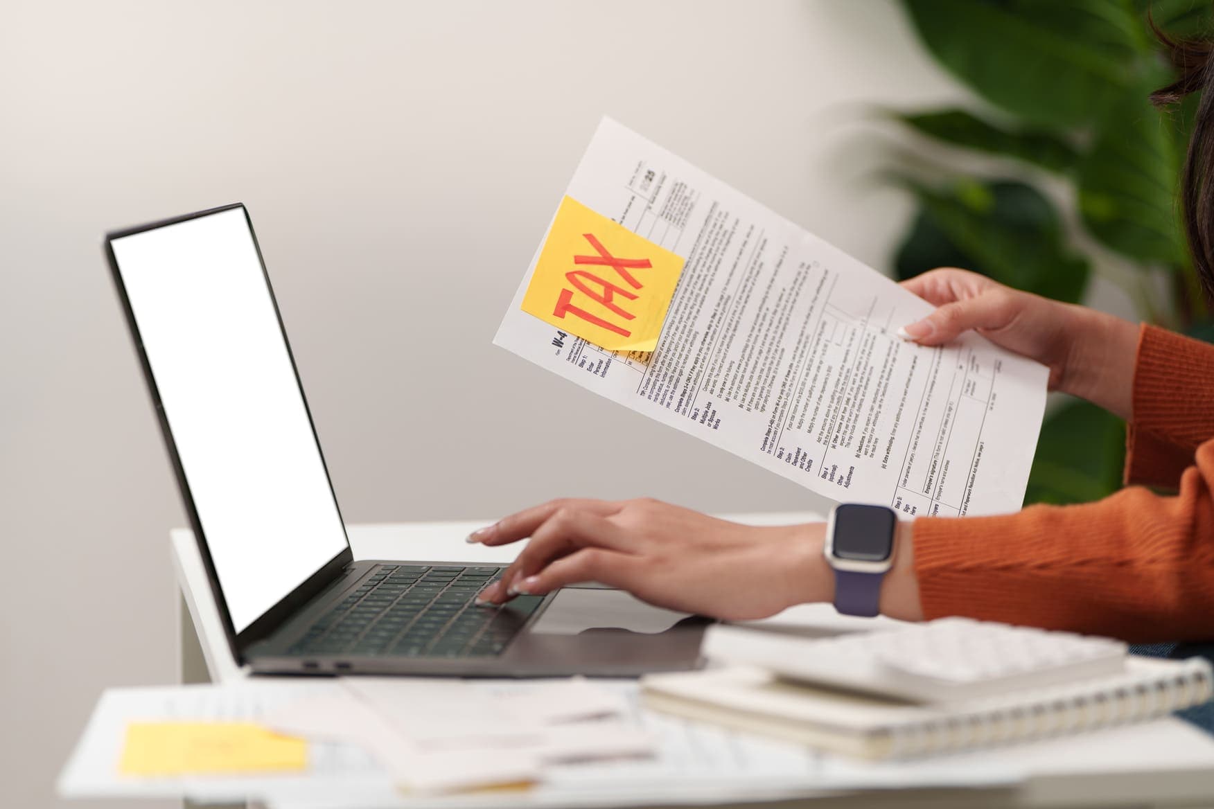Hands holding a Form W-4 with a tax note beside a laptop